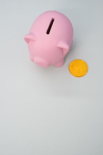 A high angle shot of a coin and a porcelain piggy bank isolated on a white background