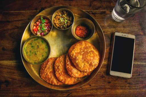A top view of South Indian different dishes on a metal tray with a phone on a wooden table