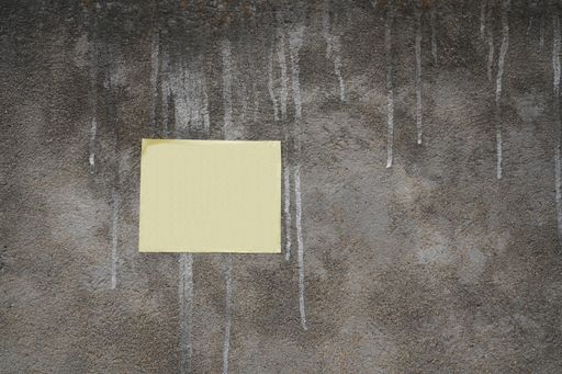 An old wall with white paint staining it and a yellow sticky note with copy space in it