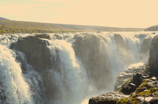 A stunning aerial view of a large waterfall cascading down a hillside in an idyllic natural setting with lush greenery and sparse vegetation