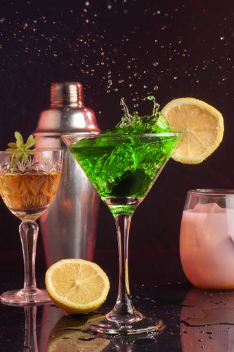 A vertical closeup shot of a green cocktail with splashes rising from the glass and spilling on the table