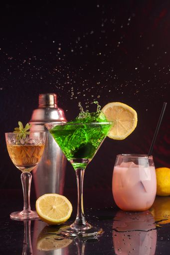 A vertical shot of a glass of green cocktail with liquid splashing and spilling on the table