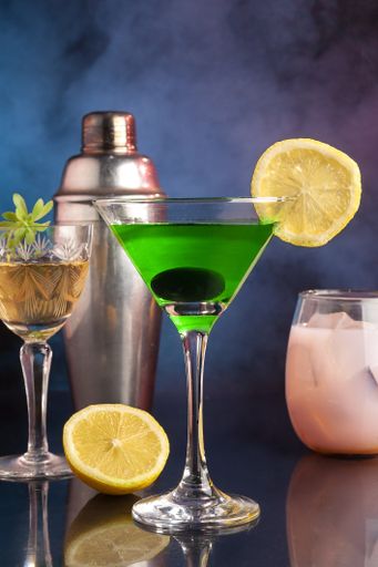 A closeup of a glass filled with green cocktail garnished by a lemon slice and an olive