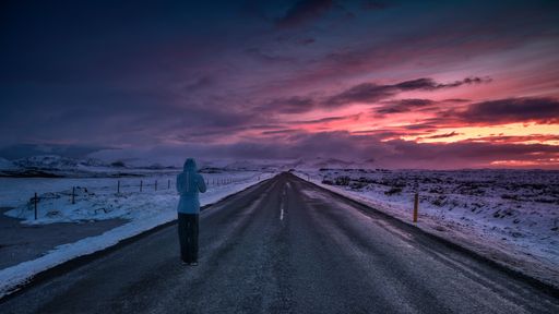 A woman standing on an empty street during a breathtaking pink sunset
