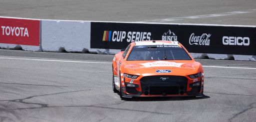 High-speed race car driving along a track in a bright orange color