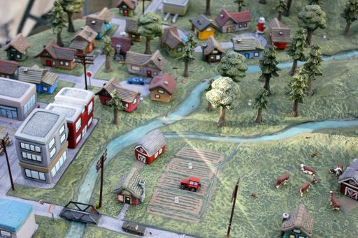 A detailed miniature toy village with roads, buildings, and a charming farm