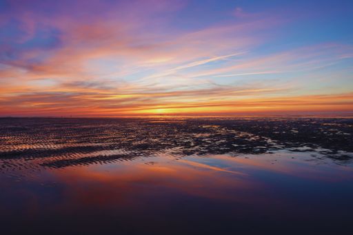 A stunning sunrise on the beach with a few wispy clouds in the sky.