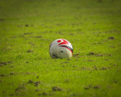 A soccer ball on a grassy field, its white and red paneled surface illuminated by the sun