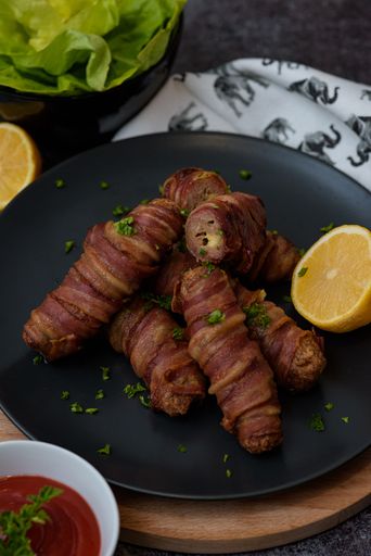 A closeup shot of stuffed bacon rolls with fresh sliced lemons and herbs on a round stone plate