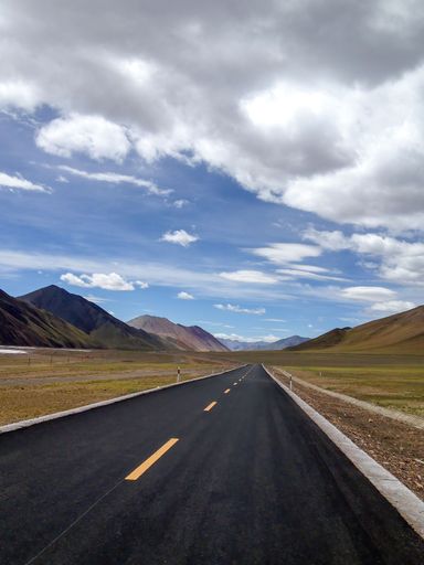 A scenic view of a winding highway snaking through a landscape of mountains and plains, set against a backdrop of cloudy skies