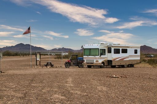 A recreational vehicle parked in a sandy desert landscape next to an American flag