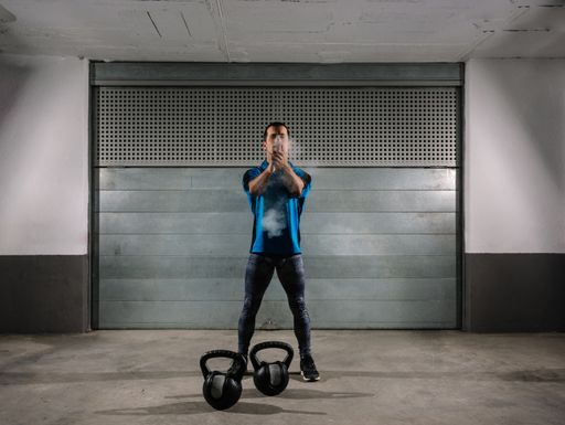 A full body shot of a Spanish male athlete using gym chalk before lifting heavy kettlebells