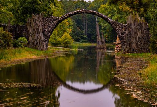 A scenic bridge known as the Rakotzbrucke, or 'devil's bridge', is surrounded by a lush forest, providing a tranquil atmosphere