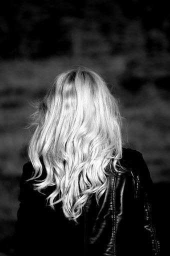 A vertical grayscale shot of a female with long blonde hair from her back