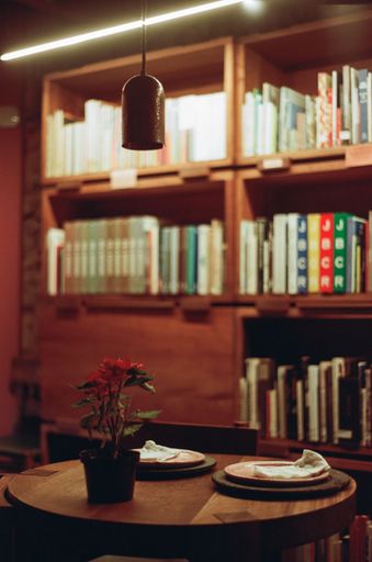 A close-up image of a wooden table with a vase of fresh pink flowers in front of a library