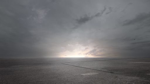A stunning view of a cloudy sky with shades of gray, over a blacktop asphalt road