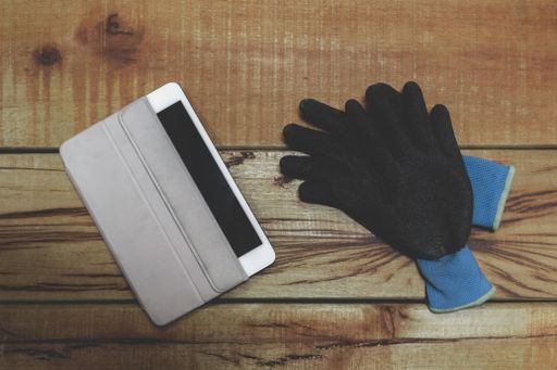 A pair of working gloves and a partially uncovered blank tablet on a wooden workbench