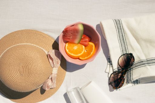 Assorted fruits in a pink bowl with a hat and sunglasses on a white fabric background