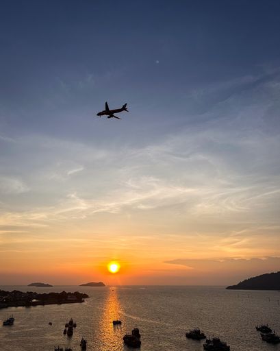 A picturesque view of a sun setting over a vast body of water, with a small airplane flying through the sky in the background