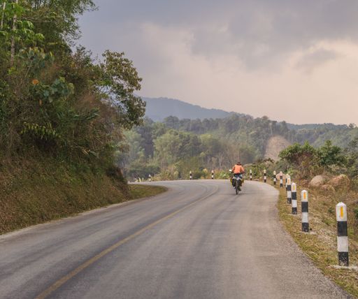 A male motorcyclist is seen riding down a hill on a dirt road