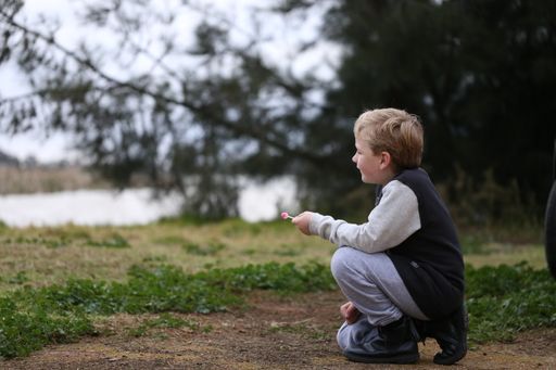 A cute young boy with a lollipop is resting on the ground in the park