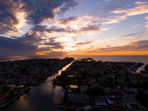 A tranquil scene of a lake surrounded by homes at sunset, with the sun casting a beautiful, golden hue over the landscape