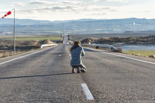 A rear view of a woman taking a photo on an empty road
