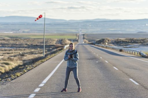 A beautiful woman holding a camera taking a photo on an empty road