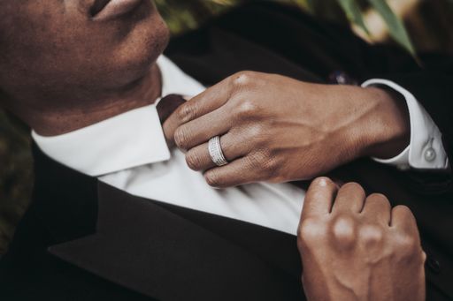 A closeup of an African-American male wearing a ring and a black suit jacket fixing his necktie