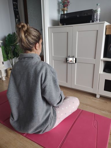 Detail of a young girl doing relaxation yoga at home, she is on top of a pink mat and watching a class on her mobile