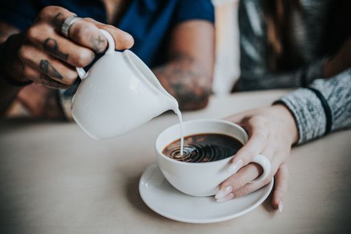 A closeup shot of a male pouring milk into female's coffee