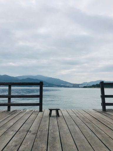 A wooden pier overlooking a majestic mountain range in the distance with the ocean in the foreground