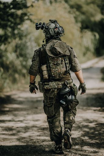 A Caucasian male dressed in a full military uniform stands with a backpack on his back