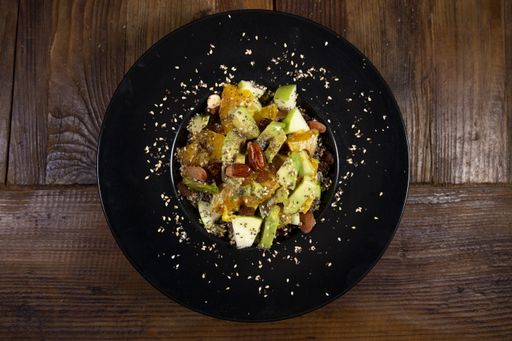 A close up shot of fruit salad with green apple, almonds, oranges and sesame seeds, black plate on rustic wooden background
