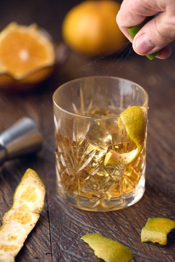 A vertical shot of a bartender putting lime in a glass of cocktail drink