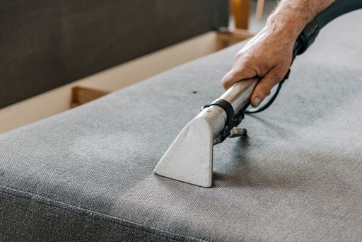 Man holding professional deep clean machine and cleaning couch in living room in apartment.