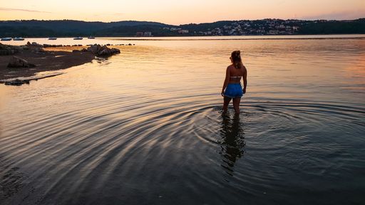 Woman walking in the water at a beach, in bikini, at sunset, on the coast of Krk island, on a sunny, summer evening. in Croatia