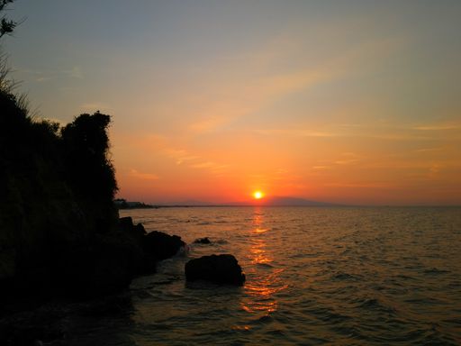 A closeup shot of a silhouette of a cliff near the ocean under a sunset sky
