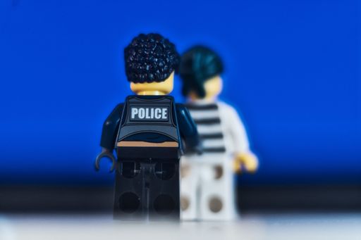 Lego figure of a police officer standing in front of blue background. Police and justice system concept