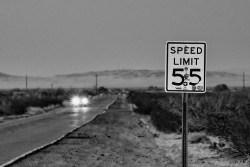 A vintage speed limit sign standing in the desert at dusk with a backdrop of the setting sun and a backdrop of desert dunes