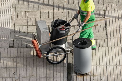 A sweeper worker pushing a cart on a city sidewalk. Urban cleaning service