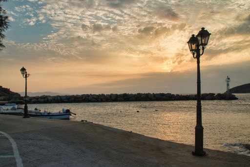 Two metal light poles stand on a beach at the edge of a bay at sunset