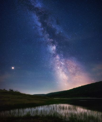 A beautiful scenery of Milky Way galaxy in the night sky over a lake in a grassy field