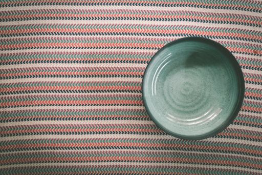 A high angle shot of an empty green bowl on a striped fabric