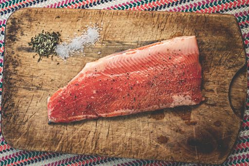 A high angle shot of raw salmon with seasonings on a wooden chopping board