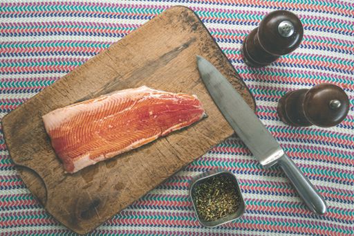 A high angle shot of raw salmon on a chopping board with a knife and different seasonings