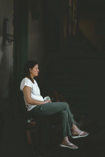 A vertical shot of a sad Caucasian female sitting on a chair holding a cup with a thoughtful face