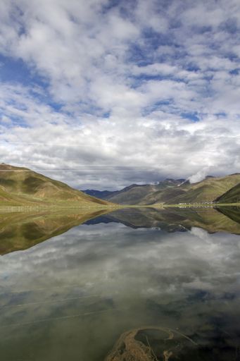 This image features a tranquil landscape of a lake reflecting the soft, fluffy clouds that drift across the sky