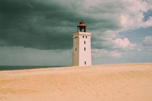 A stunning shot of a small lighthouse located on a beach, with a turbulent sky overhead creating a dramatic scene