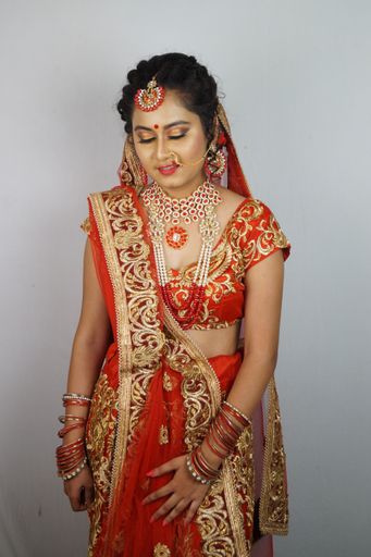 A beautiful Indian woman in a traditional red sari dress posing against a white wall